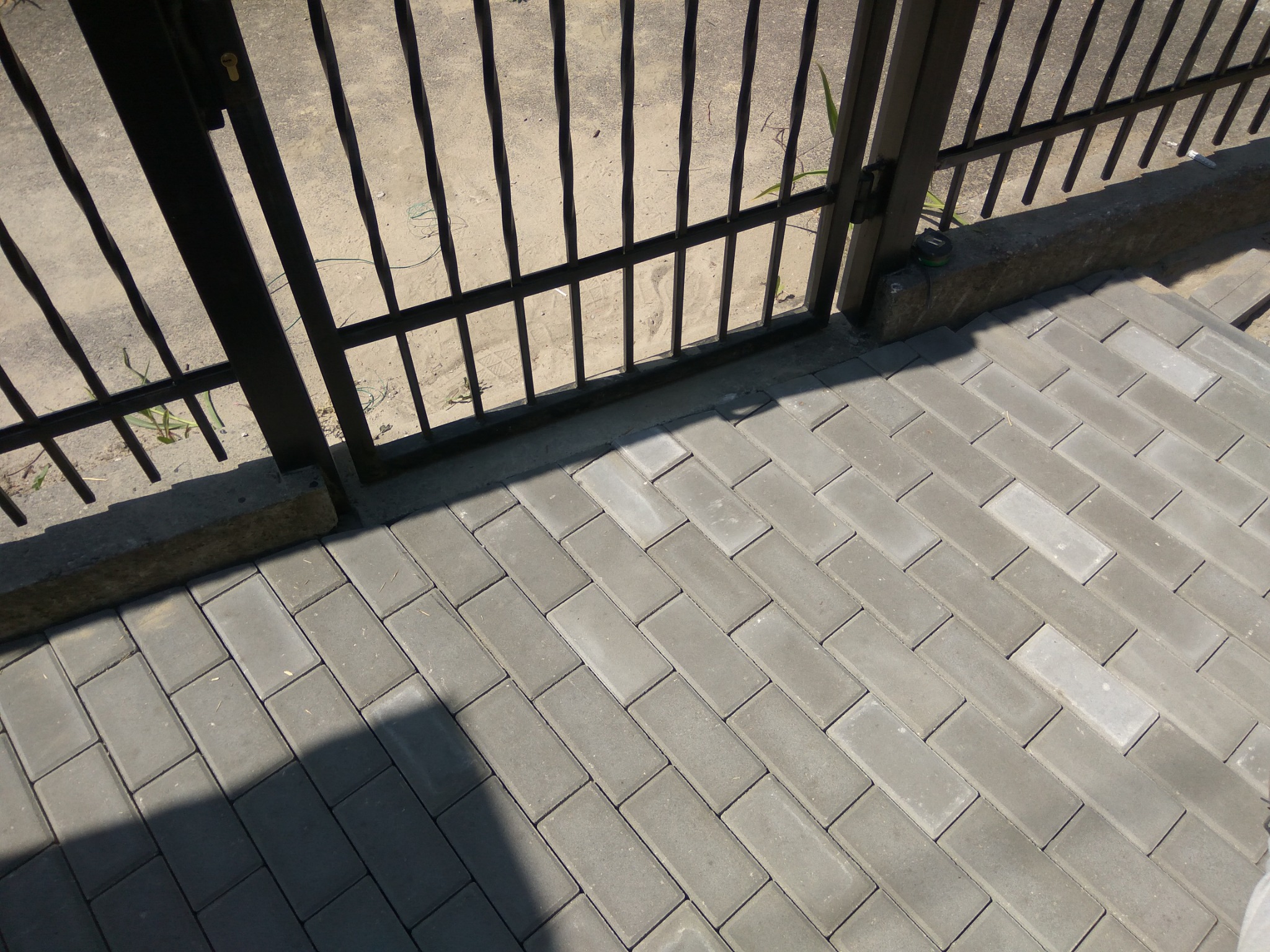 Ułożona szara kostka brukowa w jodełkę przy czarnym metalowym ogrodzeniu w Radzyminie, widok z góry.
