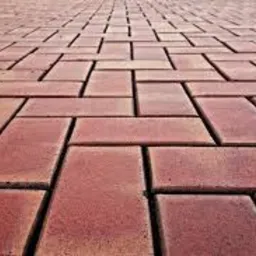 Czerwona kostka brukowa ułożona we wzór jodełki, widok z niskiej perspektywy, z efektem głębi ostrości.