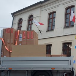 PHU SEBMARK Marek Olejnik - Dostawa okien dachowych Velux na pace samochodu dostawczego firmy Sebmark, na tle budynku z polską flagą.