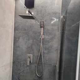 Maciej Osadowski - Nowoczesna kabina prysznicowa z deszczownicą i baterią podtynkową, wykończona płytkami w odcieniach szarości, oświetlenie LED podsufitowe.