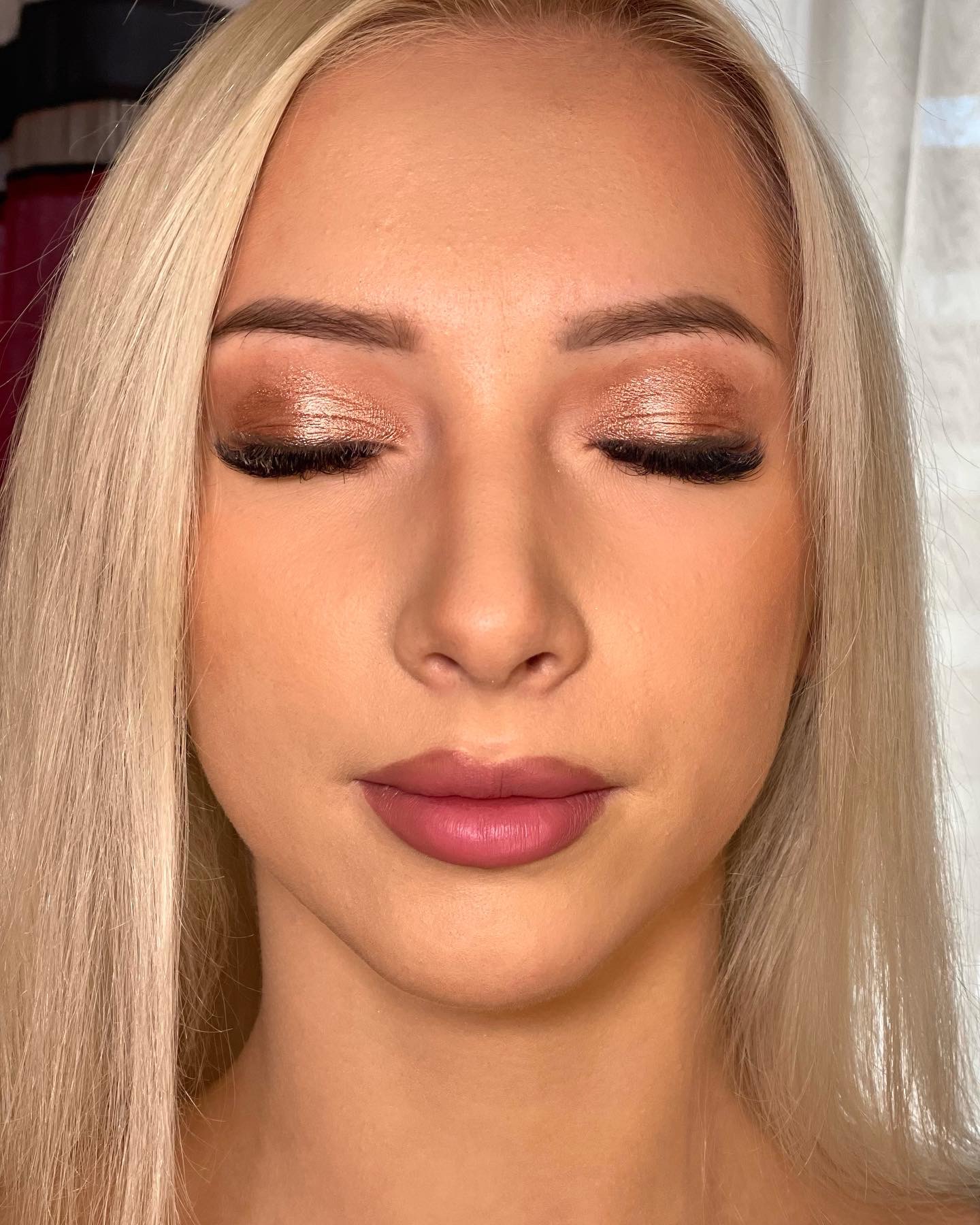 Portret kobiety z zamkniętymi oczami, prezentujący metaliczny, brązowo-złoty cień do powiek z wyraźnie zaznaczonymi rzęsami i delikatnie podkreślonymi ustami w odcieniu różu.