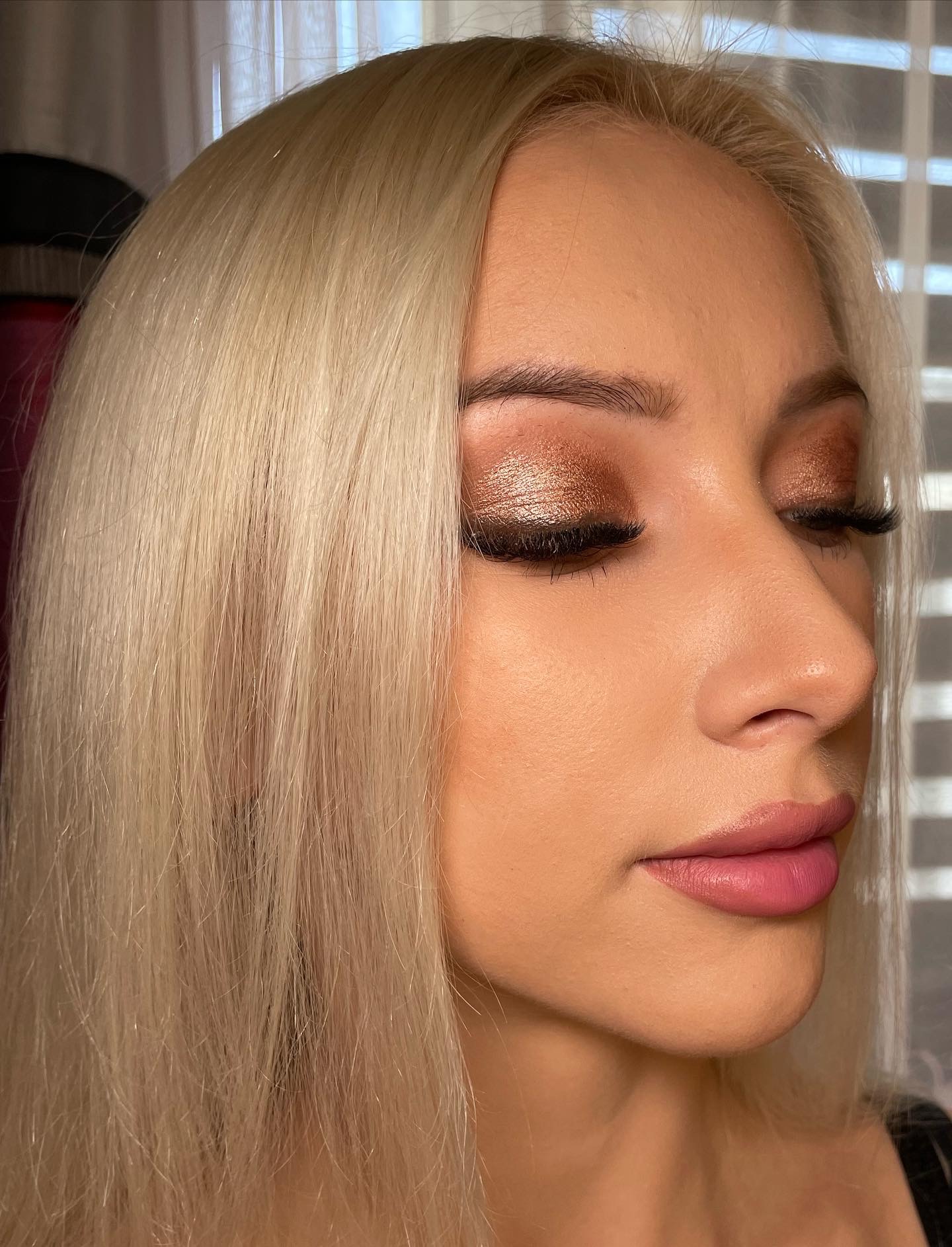 Portret kobiety z platynowymi włosami i profesjonalnym makijażem oczu w odcieniach brązu z wyraźnie zaznaczonymi rzęsami i różowymi ustami, wykonany w zbliżeniu.