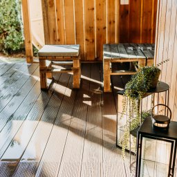 Mega Moc Paweł Drzeżdzon - Drewniana konstrukcja z siedziskami z palet i dekoracyjną latarnią oraz rośliną w doniczce, podłoga z desek kompozytowych, widoczne refleksy światła na podłodze.