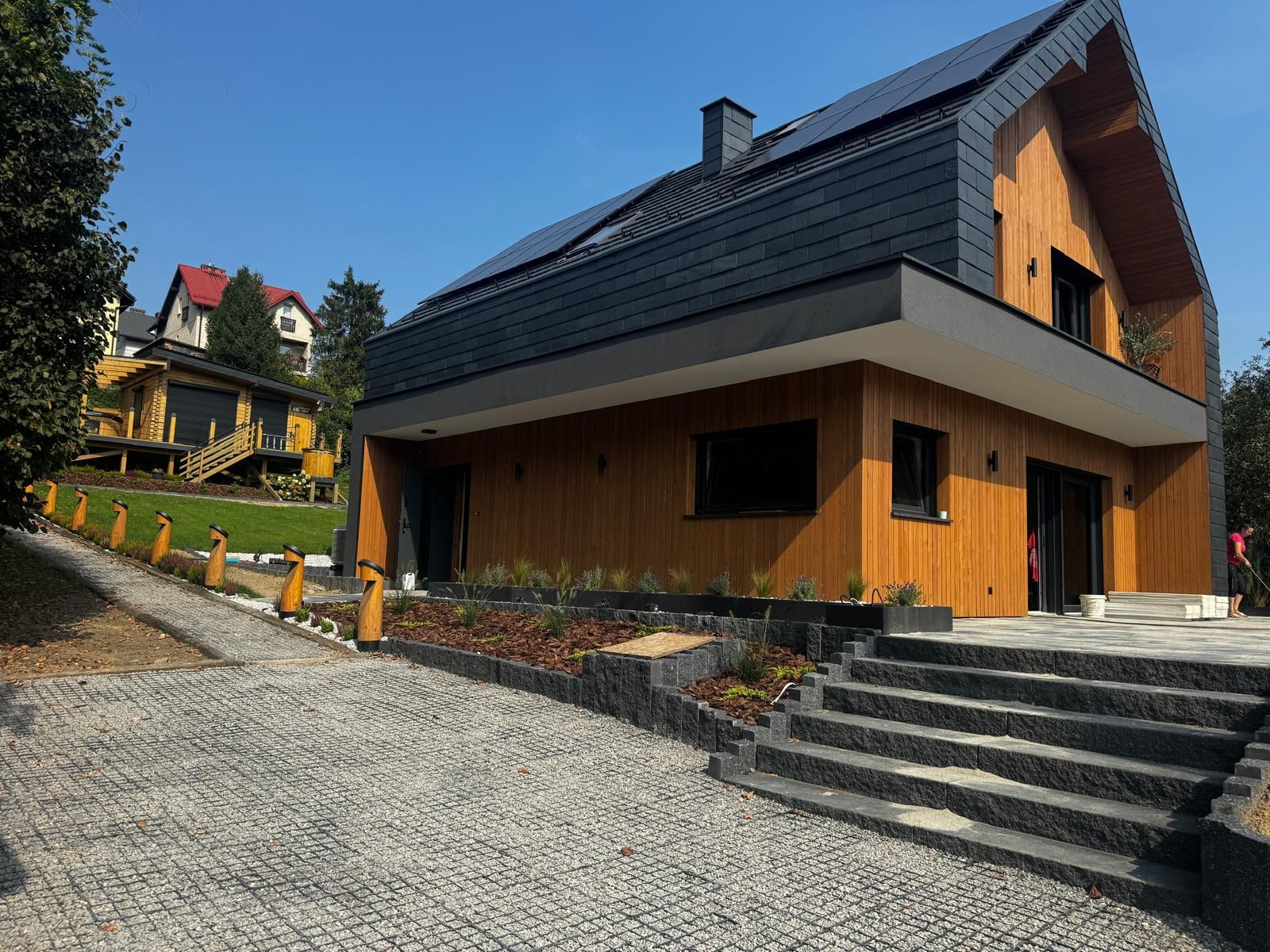 Nowoczesny dom jednorodzinny z drewnianą elewacją i ciemnym dachem w Turzy Śląskiej, widok z kamiennego podjazdu.