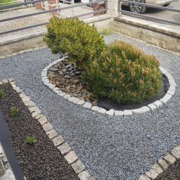Firma Handlowo-Usługowa Dominik Smarzoch - Ogródek z dwoma karłowatymi sosnami otoczonymi kamieniami, wysypany szarym żwirem, z obrzeżem z kostki granitowej, w tle zaparkowane samochody.