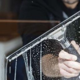 Waldemar Dondajewski - Ręka z czarnym ściągaczem do szyb usuwa pianę z mytej szyby, widoczne krople spływają po szkle.