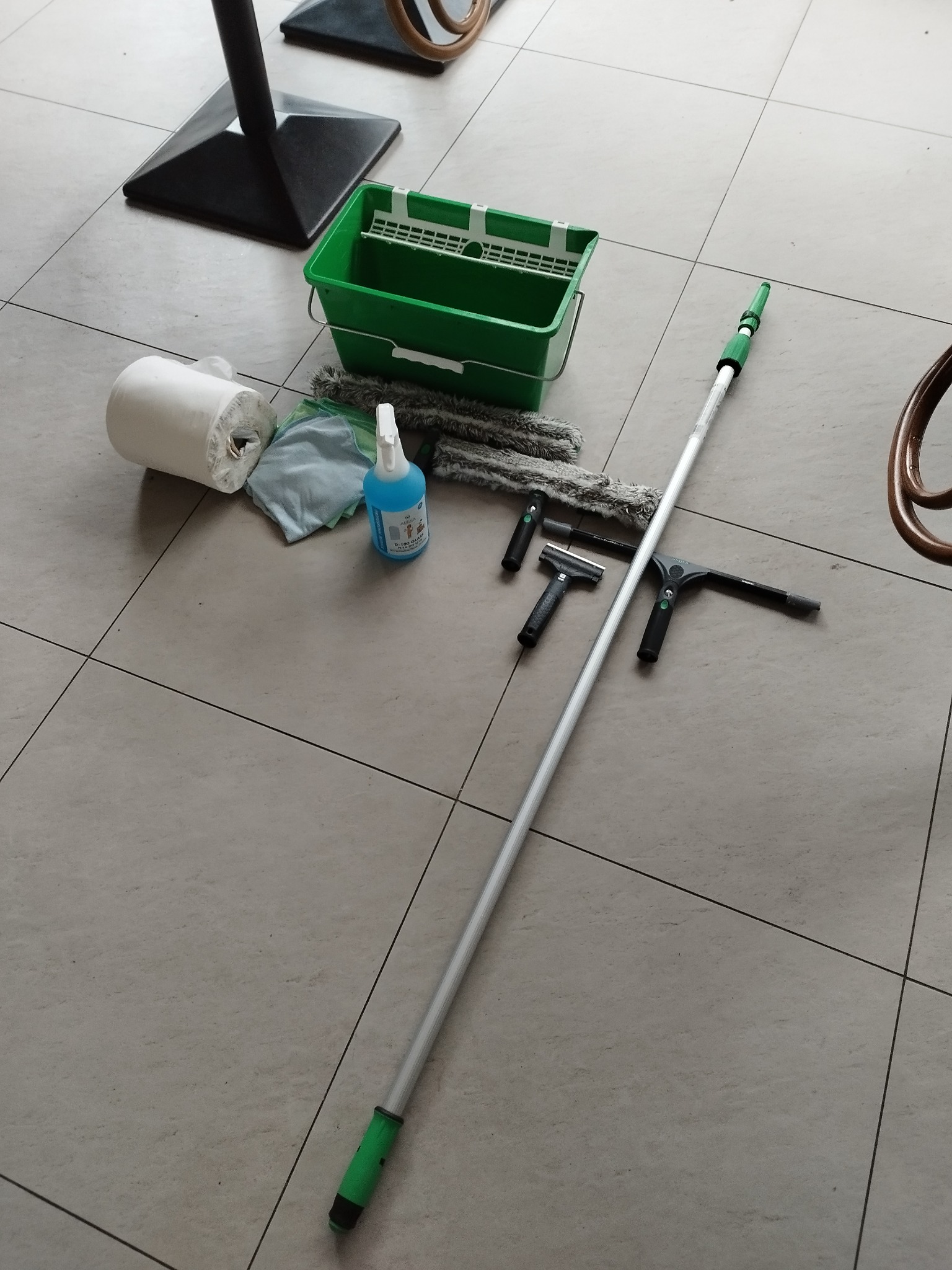 Zestaw narzędzi do czyszczenia powierzchni płaskich: wiadro z wkładem, rolka papieru, spryskiwacz z płynem, ściereczki, teleskopowy kij i różne rodzaje ściągaczek do wody, ułożone na szarej...