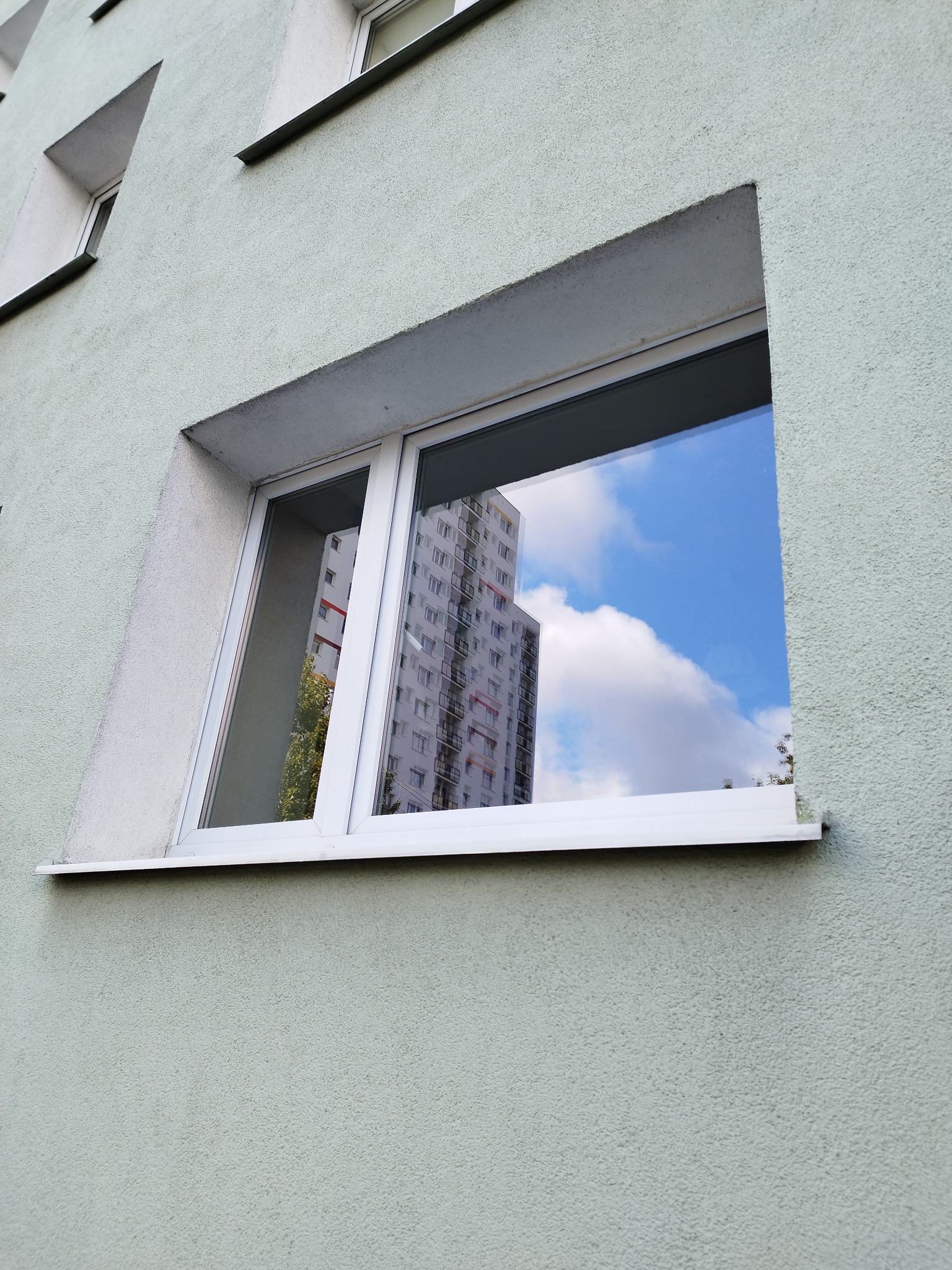 Okna w bloku z odbiciem budynku i błękitnego nieba z chmurami.