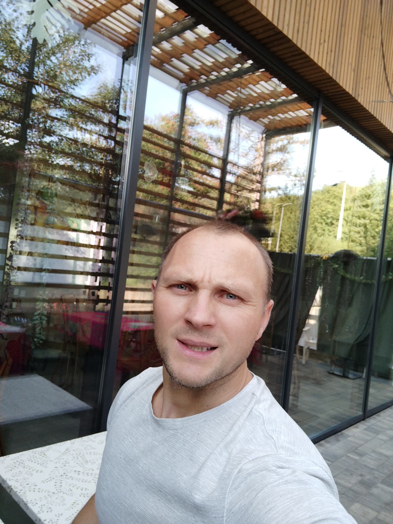 Mężczyzna pozuje na tle nowoczesnego budynku z dużymi, czystymi oknami, w których odbija się otoczenie.