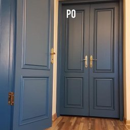 SERWIS I RENOWACJA „ANTA” - Niebieskie, dwuskrzydłowe drzwi wewnętrzne z ozdobnymi ramkami i złotymi klamkami, widoczne po renowacji, na tle drewnianej podłogi. Częściowo otwarte drzwi po lewej.