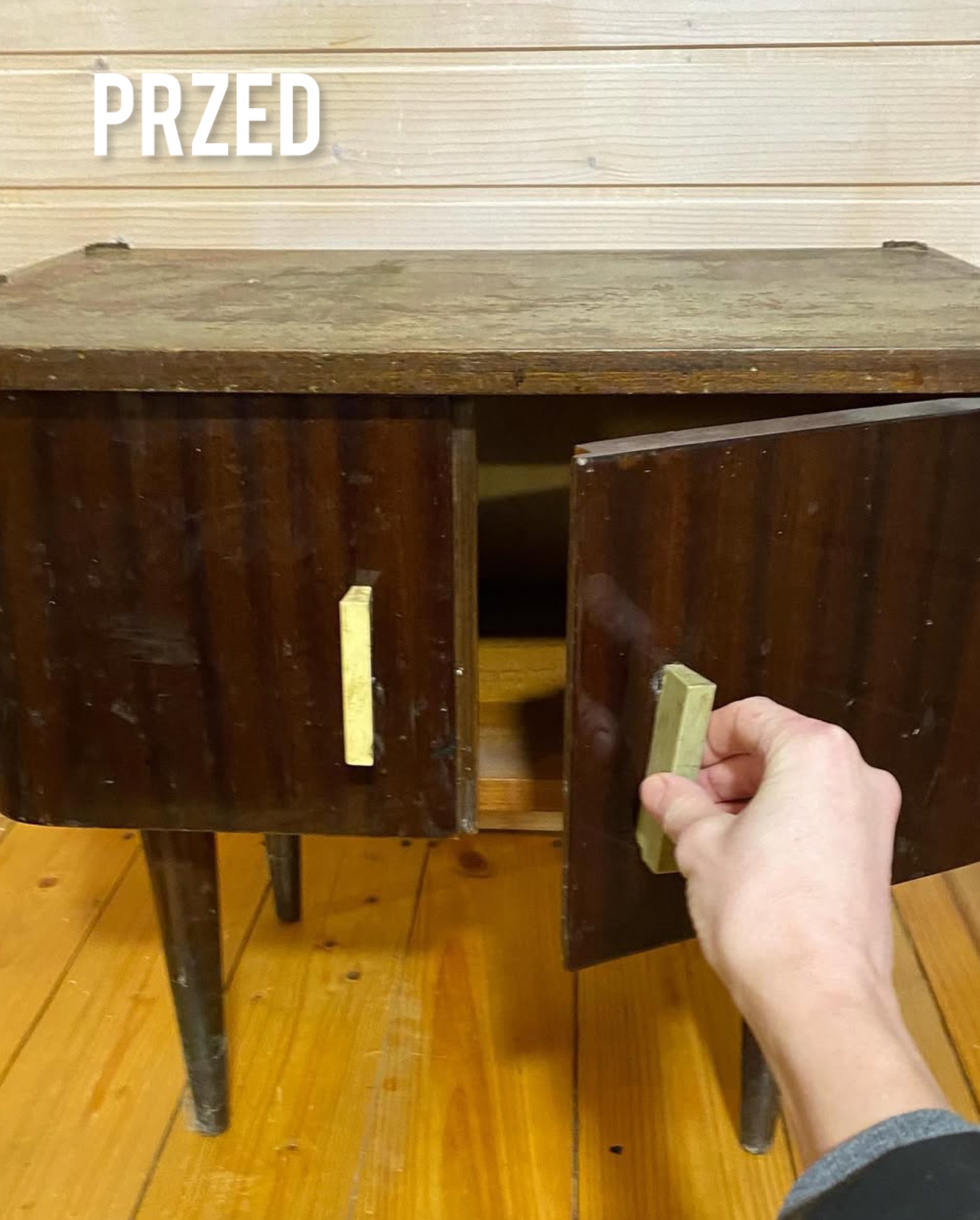 Zdjęcie szafki nocnej przed renowacją. Widoczne uszkodzenia i odbarwienia na ciemnym drewnie, uchwyty w kolorze złotym. Na górze napis 'PRZED'.