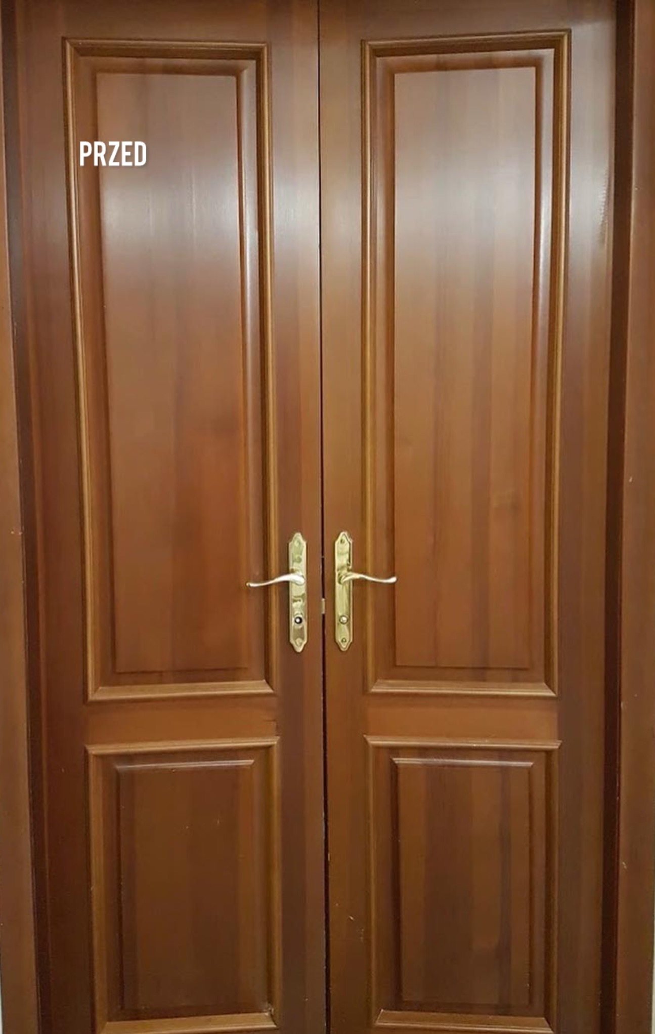 Brązowe, drewniane drzwi dwuskrzydłowe z złotymi klamkami w ujęciu z przodu. Na lewym skrzydle widnieje napis 'PRZED'.