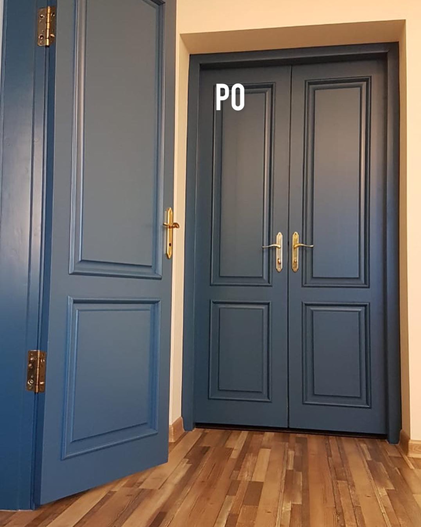 Niebieskie, dwuskrzydłowe drzwi wewnętrzne z ozdobnymi ramkami i złotymi klamkami, widoczne po renowacji, na tle drewnianej podłogi. Częściowo otwarte drzwi po lewej.