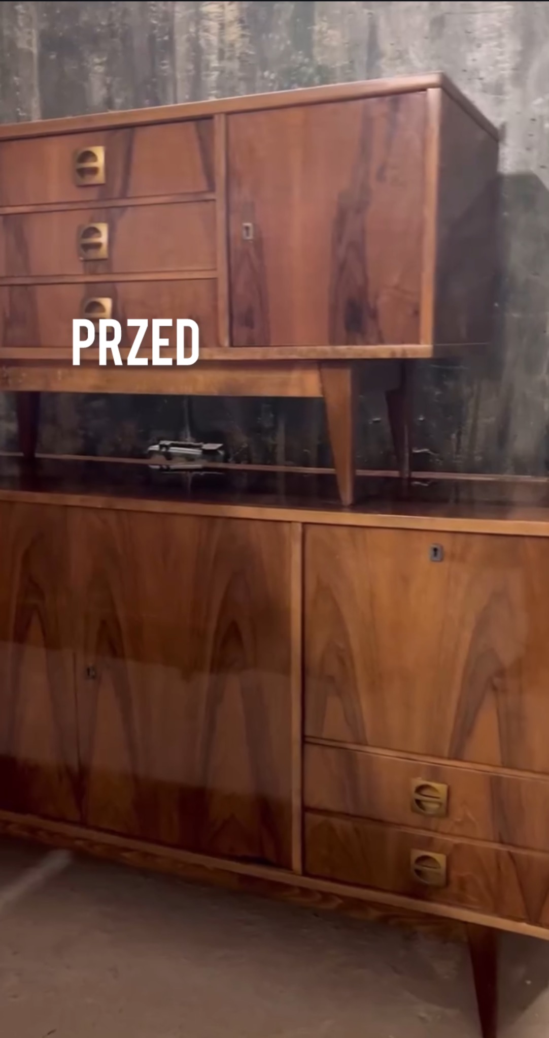 Antyczny, dwuczęściowy kredens z forniru orzechowego w stylu vintage, z charakterystycznymi, mosiężnymi uchwytami, sfotografowany przed renowacją.