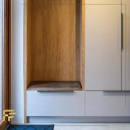 Nowoczesna zabudowa meblowa z siedziskiem wnękowym wykończonym drewnem, połączona z szafą o gładkich, jasnych frontach.