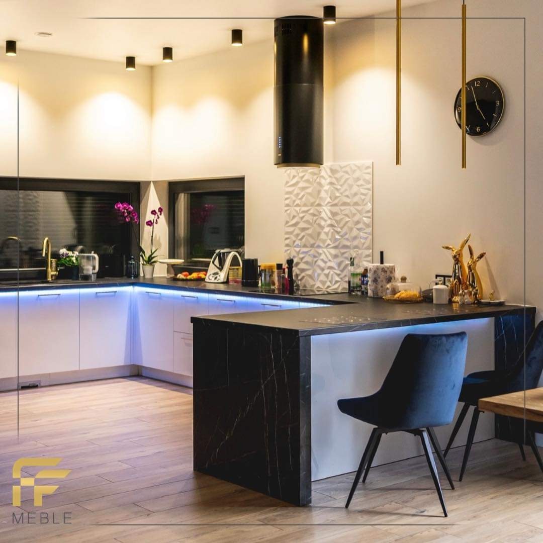 Nowoczesna kuchnia z białymi szafkami, czarnym blatem z marmurowym wzorem, podświetleniem LED, czarnym okapem cylindrycznym i dekoracyjną ścianą 3D.