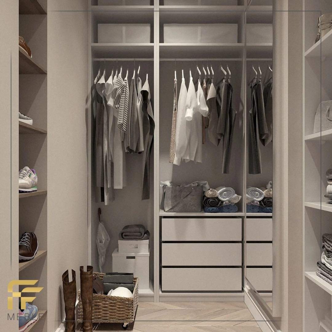 Wnętrze garderoby z białymi szafami na wymiar, ubraniami na wieszakach, półkami na buty i koszem z akcesoriami na drewnianej podłodze.