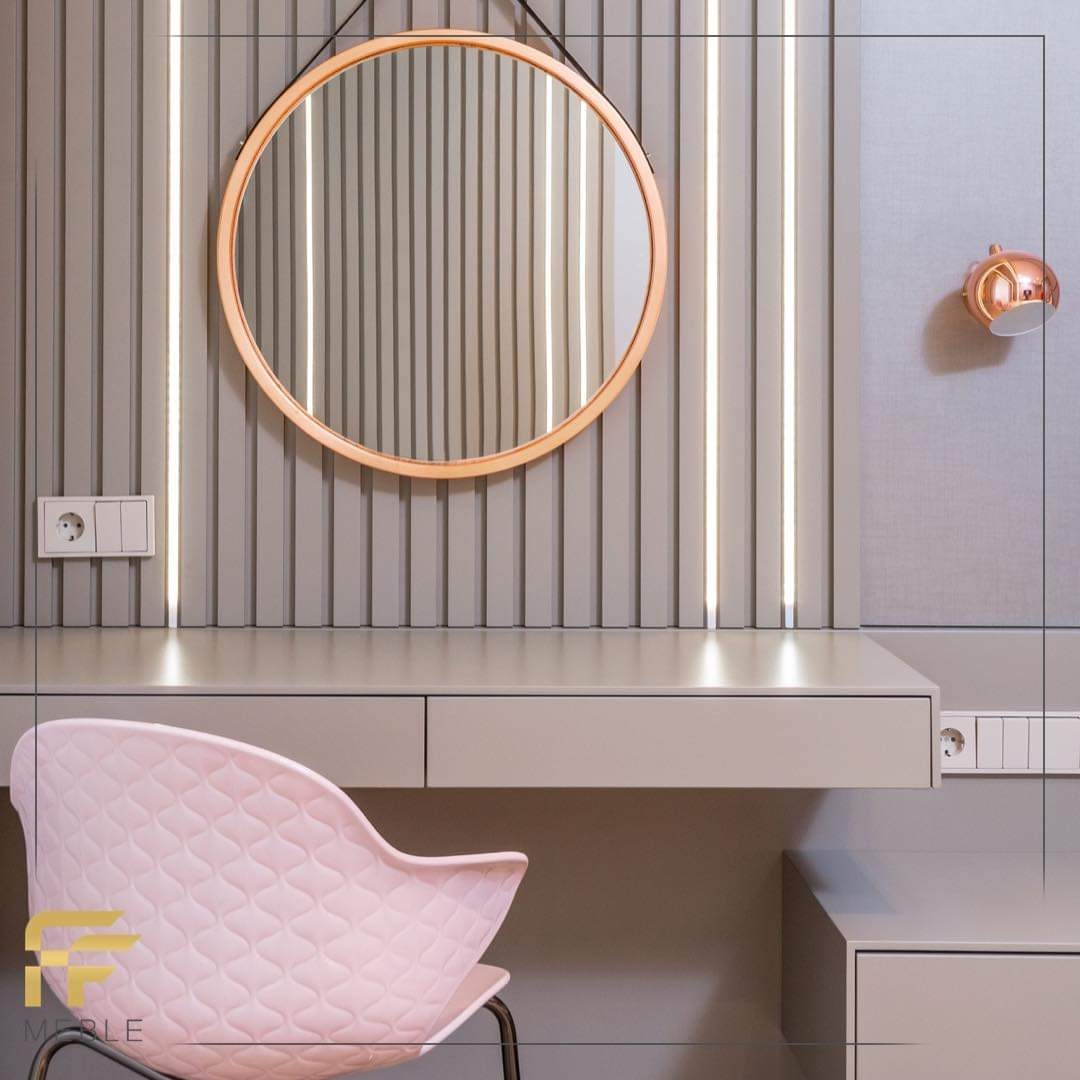 Szaro-różowa toaletka z okrągłym lustrem w miedzianej ramie, oświetleniem LED w tle i tapicerowanym krzesłem z pikowaniem.