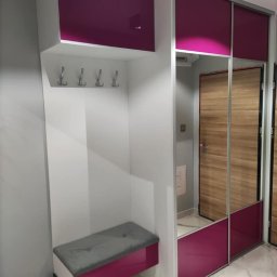 AgaMeble - Biała szafa wnękowa z przesuwnymi drzwiami lustrzanymi i fuksjowymi akcentami, wbudowane siedzisko z szarą poduszką i wieszakami na ubrania.