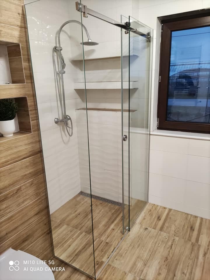 Nowoczesna kabina prysznicowa ze szklanymi drzwiami przesuwnymi, wykończona płytkami imitującymi drewno i białymi płytkami strukturalnymi, z widocznymi półkami wnękowymi.