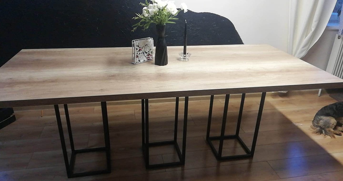 Stół z blatem imitującym drewno i metalowymi nogami w kształcie prostopadłościanów, dekoracje na stole w mieszkaniu w Warszawie.