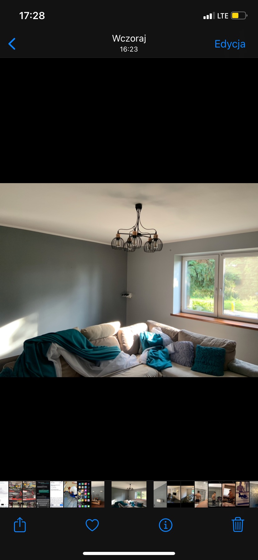 Szare ściany w pokoju przed malowaniem, zabezpieczony narożnik sofy turkusowym materiałem, widoczne gniazdko elektryczne bez obudowy i nowoczesna lampa sufitowa.