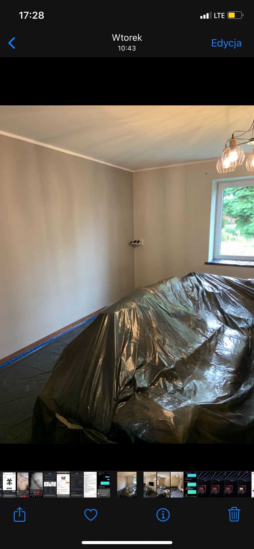 Przygotowanie do prac remontowych: pokój zabezpieczony folią malarską, szare ściany, widoczne gniazdko elektryczne i lampa w stylu industrialnym.