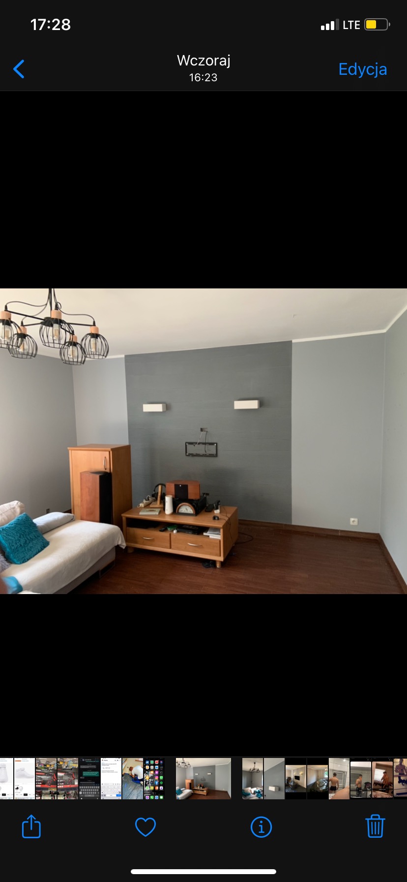 Salon w Olesnie po odświeżeniu: szara ściana z dwoma białymi kinkietami, brązowa podłoga, drewniane meble i fragment sofy z turkusową poduszką.