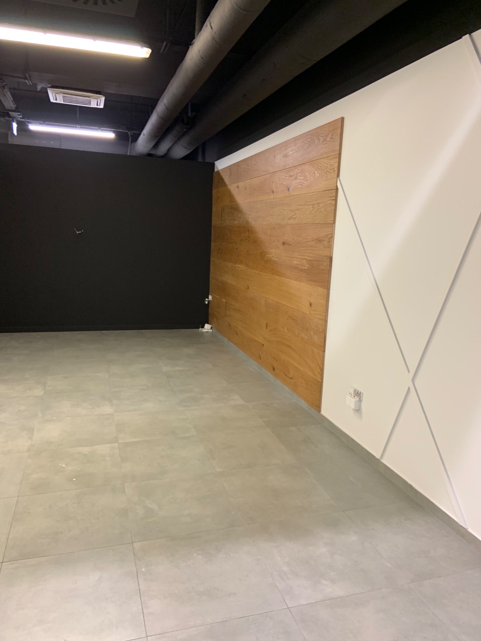 Nowoczesne wnętrze biurowe z czarną ścianą, drewnianą okładziną i białą ścianą z dekoracyjnymi listwami, szara podłoga z płytek.