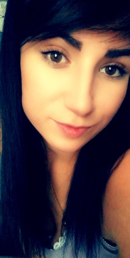 Portret młodej kobiety z ciemnymi włosami i brązowymi oczami, delikatny uśmiech, widoczny łańcuszek na szyi.