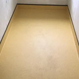 Beżowa podłoga wykończona czarną listwą przypodłogową w pomieszczeniu z szarymi ścianami, widok z góry.