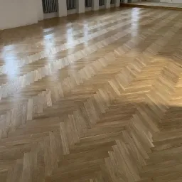 Parkiet ułożony w jodełkę w przestronnym, jasnym pomieszczeniu z grzejnikami pod oknami