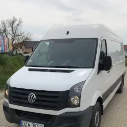 Biały samochód dostawczy Volkswagen Crafter z polską tablicą rejestracyjną DZA 3KS2, zaparkowany na kostce brukowej w pochmurny dzień.