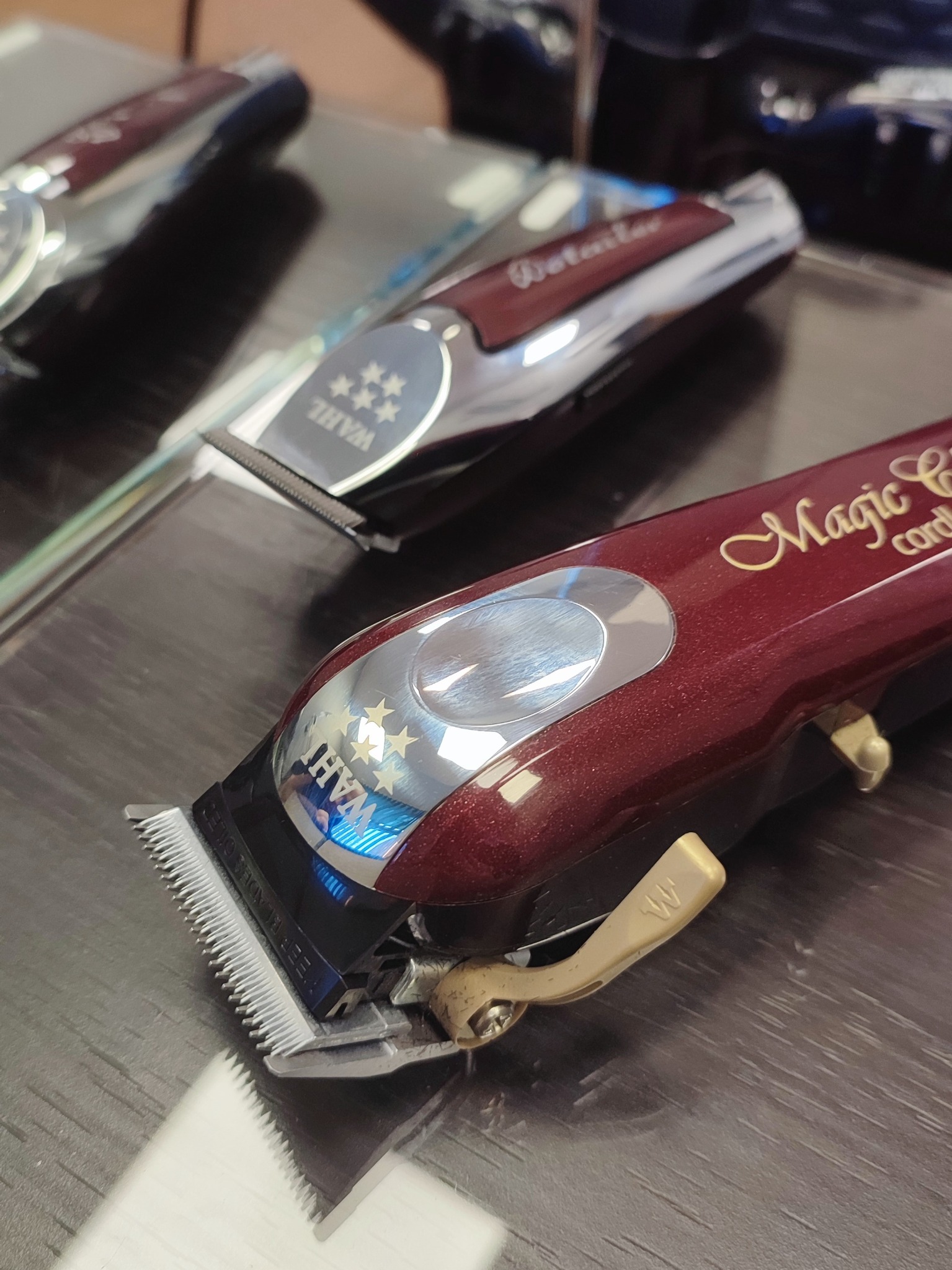 Trzy maszynki do strzyżenia włosów marki Wahl na ciemnym blacie, z bliska, widoczne ostrza i detale obudowy.