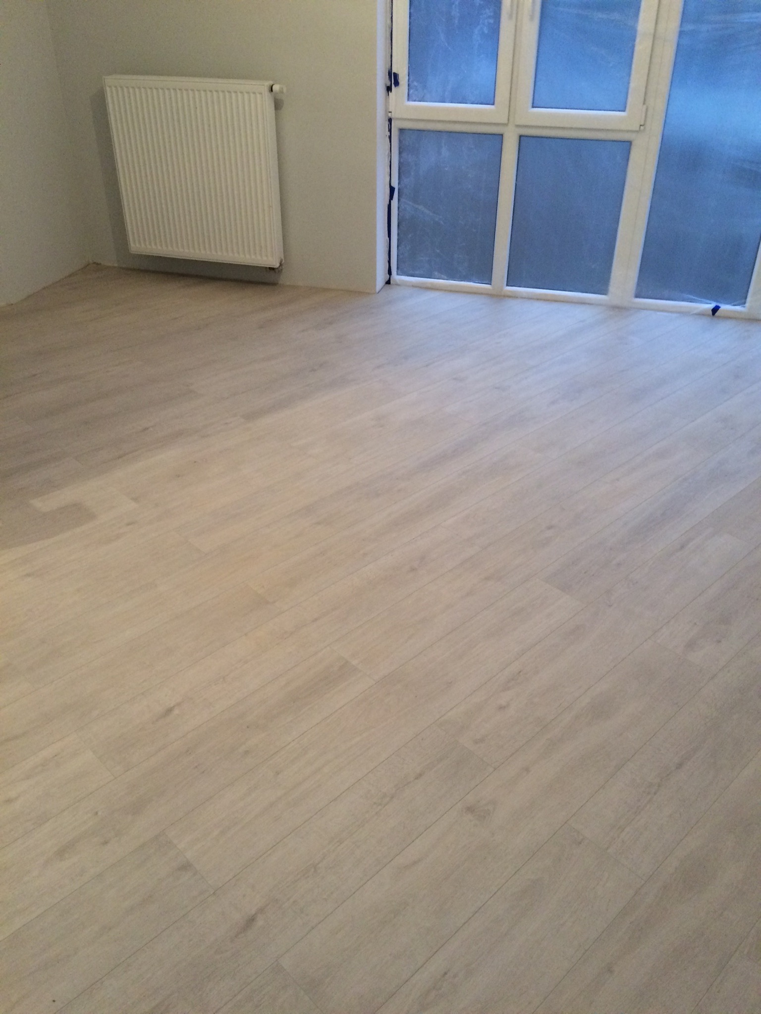 Jasna podłoga z paneli ułożona w pokoju z grzejnikiem i oknem zabezpieczonym folią malarską.