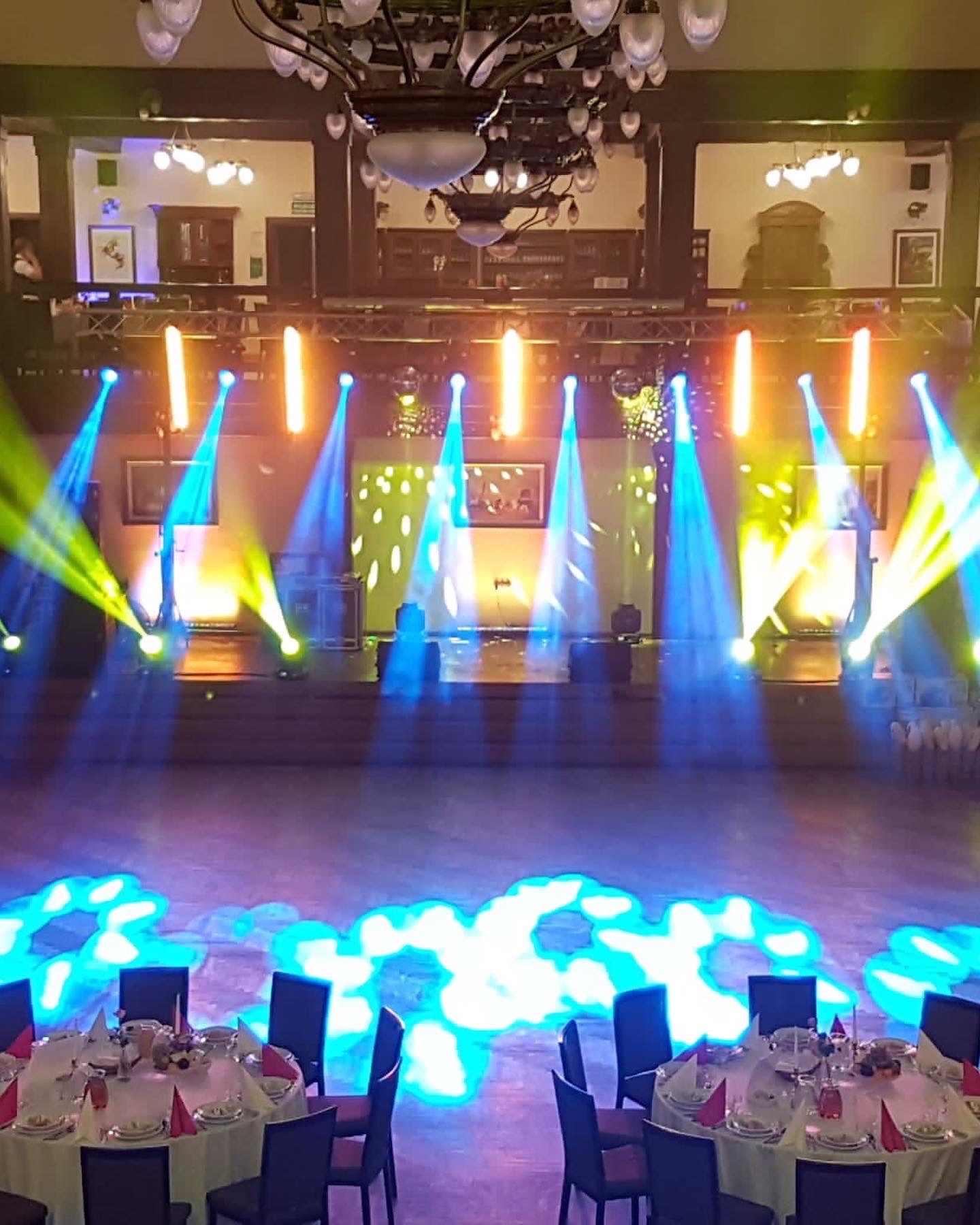 Sala balowa z oświetleniem scenicznym, stoły bankietowe z czerwonymi serwetkami w tle, parkiet oświetlony wzorami.