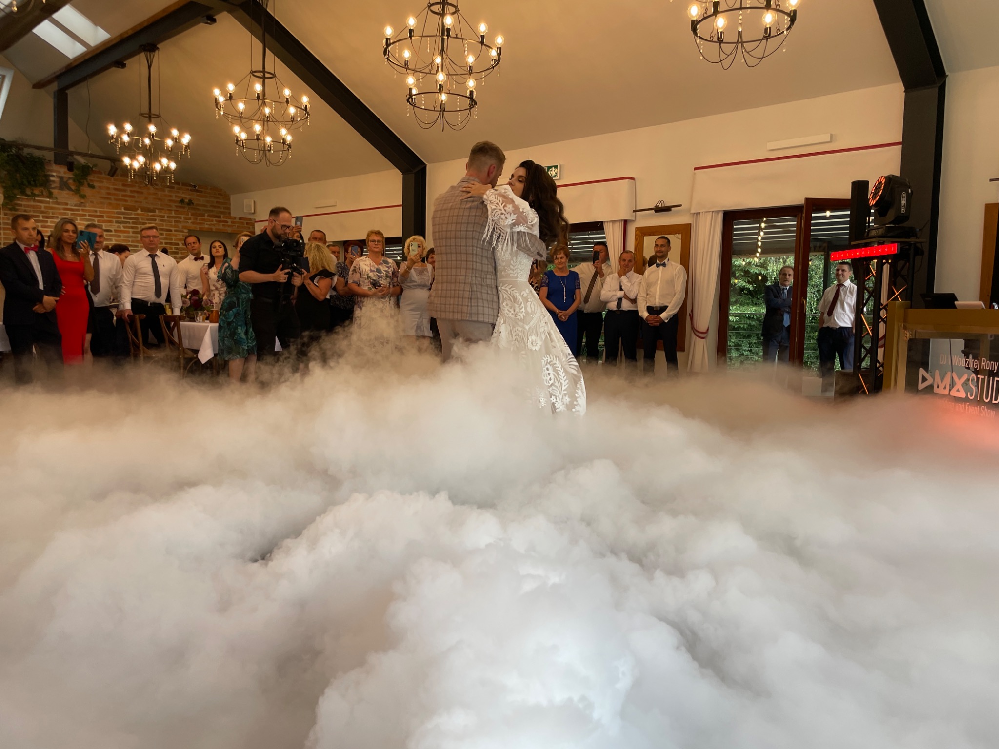Para młoda tańczy pierwszy taniec w chmurach, oświetlenie sceniczne, goście weselni obserwują.