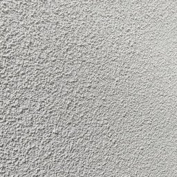 Usługi Wykończenia Wnętrz Remontowe Ogólnobudowlane Stolarskie Ciesielskie Handyman Marek Gąsiewicz - Szara, chropowata faktura ściany zewnętrznej w zbliżeniu, oświetlona z góry, ukazująca detale tynku strukturalnego w neutralnej tonacji.