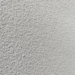 Szara, chropowata faktura ściany zewnętrznej w zbliżeniu, oświetlona z góry, ukazująca detale tynku strukturalnego w neutralnej tonacji.
