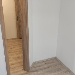 Usługi Wykończenia Wnętrz Remontowe Ogólnobudowlane Stolarskie Ciesielskie Handyman Marek Gąsiewicz - Wykończone wnętrze w Bytowie: podłoga z paneli w odcieniach drewna i białe ściany. Widoczne drzwi wewnętrzne z ościeżnicą w kolorze podłogi.