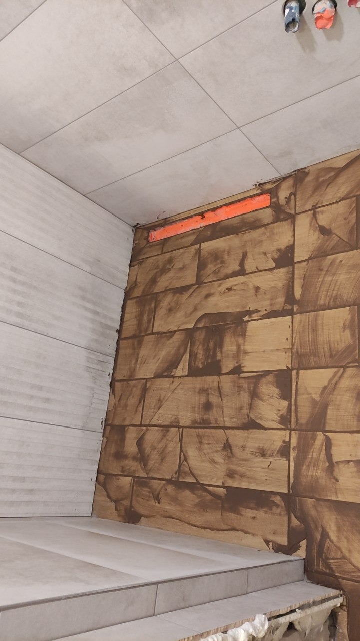 Łazienka w trakcie remontu: ułożone płytki imitujące drewno na ścianie, widoczna listwa poziomująca, białe płytki na suficie i podłodze, etap prac wykończeniowych.