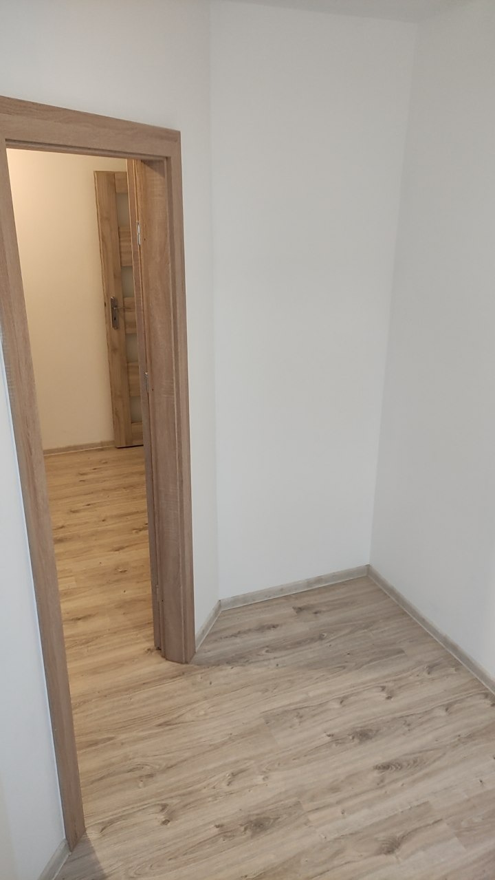 Wykończone wnętrze w Bytowie: podłoga z paneli w odcieniach drewna i białe ściany. Widoczne drzwi wewnętrzne z ościeżnicą w kolorze podłogi.