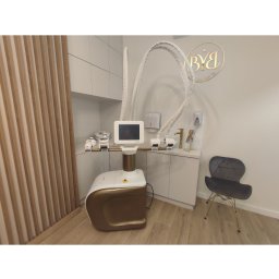 Book Your Beauty SC - Nowoczesny gabinet z urządzeniem do modelowania sylwetki w kolorze białym i złotym, obok szara krzesło na złotych nóżkach, w tle logo firmy na ścianie.