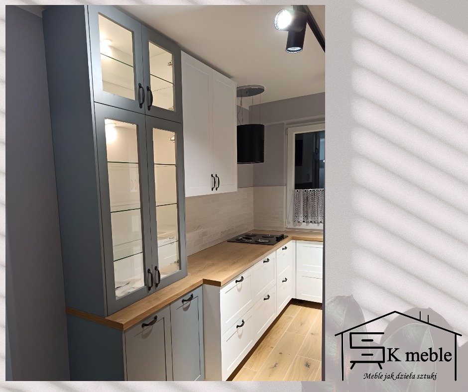 Szaro-biała kuchnia z drewnianym blatem, oświetleniem podszafkowym i przeszklonymi górnymi szafkami, widok na fragment pomieszczenia z oknem.