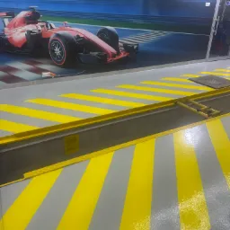 Szaro-żółta podłoga z pasami w garażu w Warszawie, z dekoracyjnym motywem bolidu Formuły 1 na ścianie w tle.