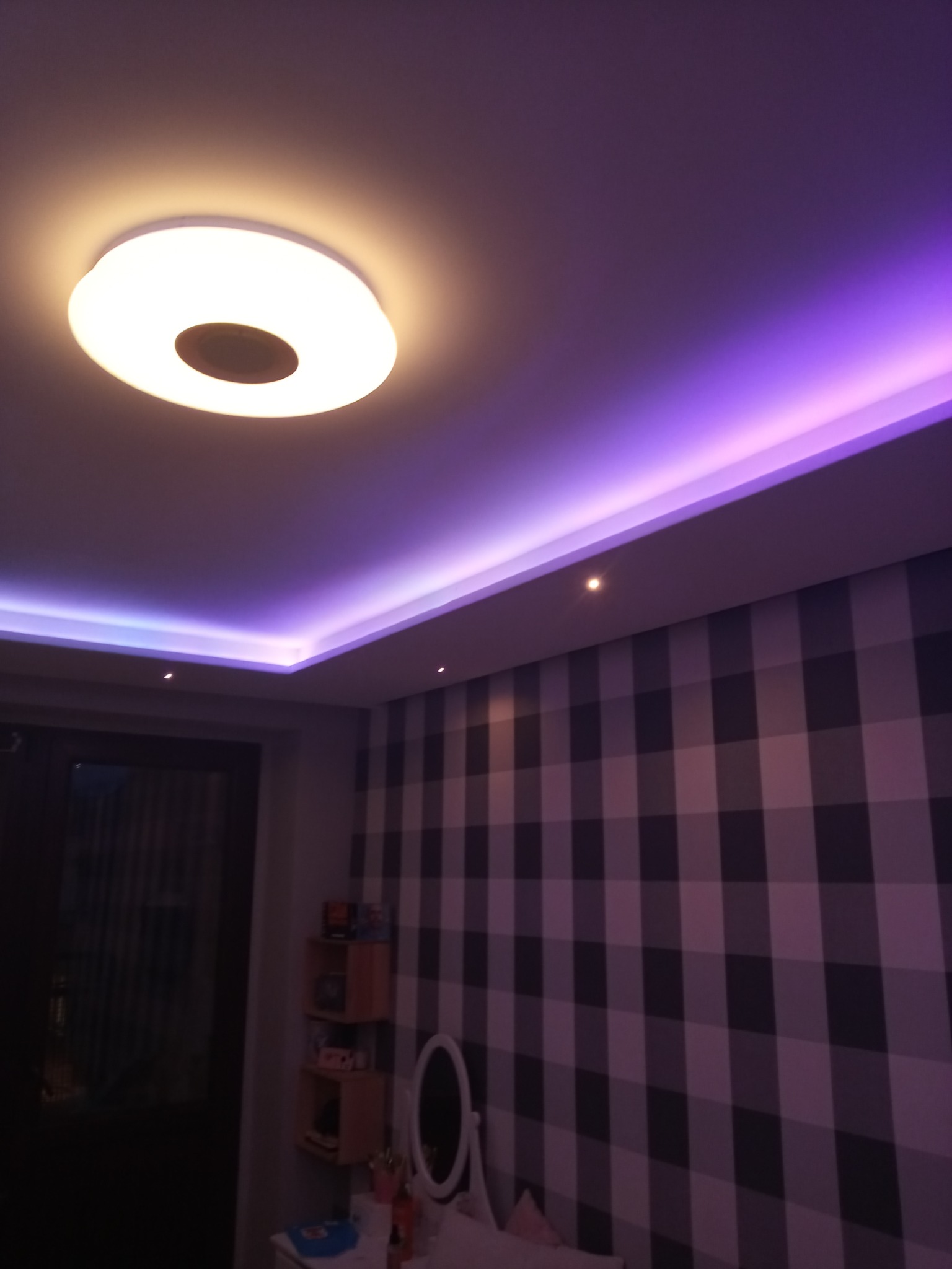 Pokój z podświetlanym sufitem w kolorze fioletowym i okrągłą lampą sufitową, ściana w kratę.