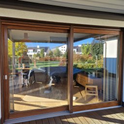 Renowacja drewna Adam Bednarski - Przesuwne, dwuskrzydłowe, drewniane drzwi tarasowe z widokiem na ogród, zamontowane na drewnianym tarasie.