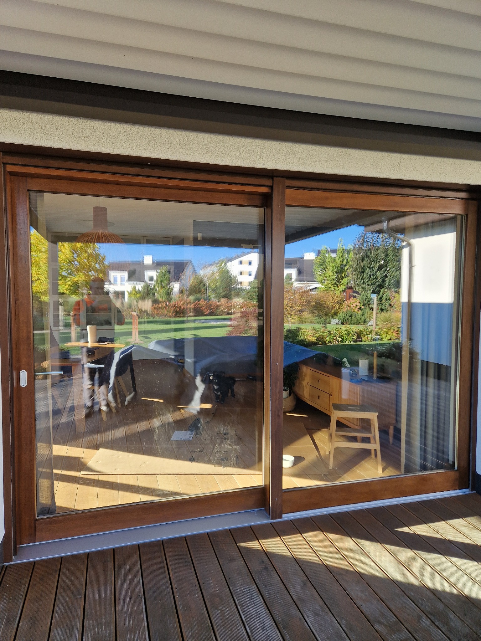 Przesuwne, dwuskrzydłowe, drewniane drzwi tarasowe z widokiem na ogród, zamontowane na drewnianym tarasie.