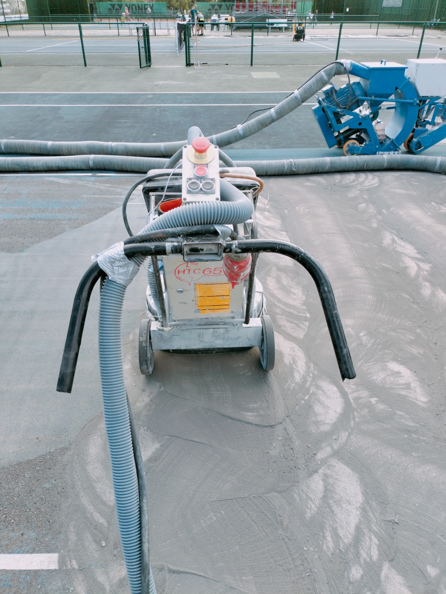 Maszyna do czyszczenia i przygotowania powierzchni kortu tenisowego z widocznymi śladami pracy i systemem odsysania pyłu.