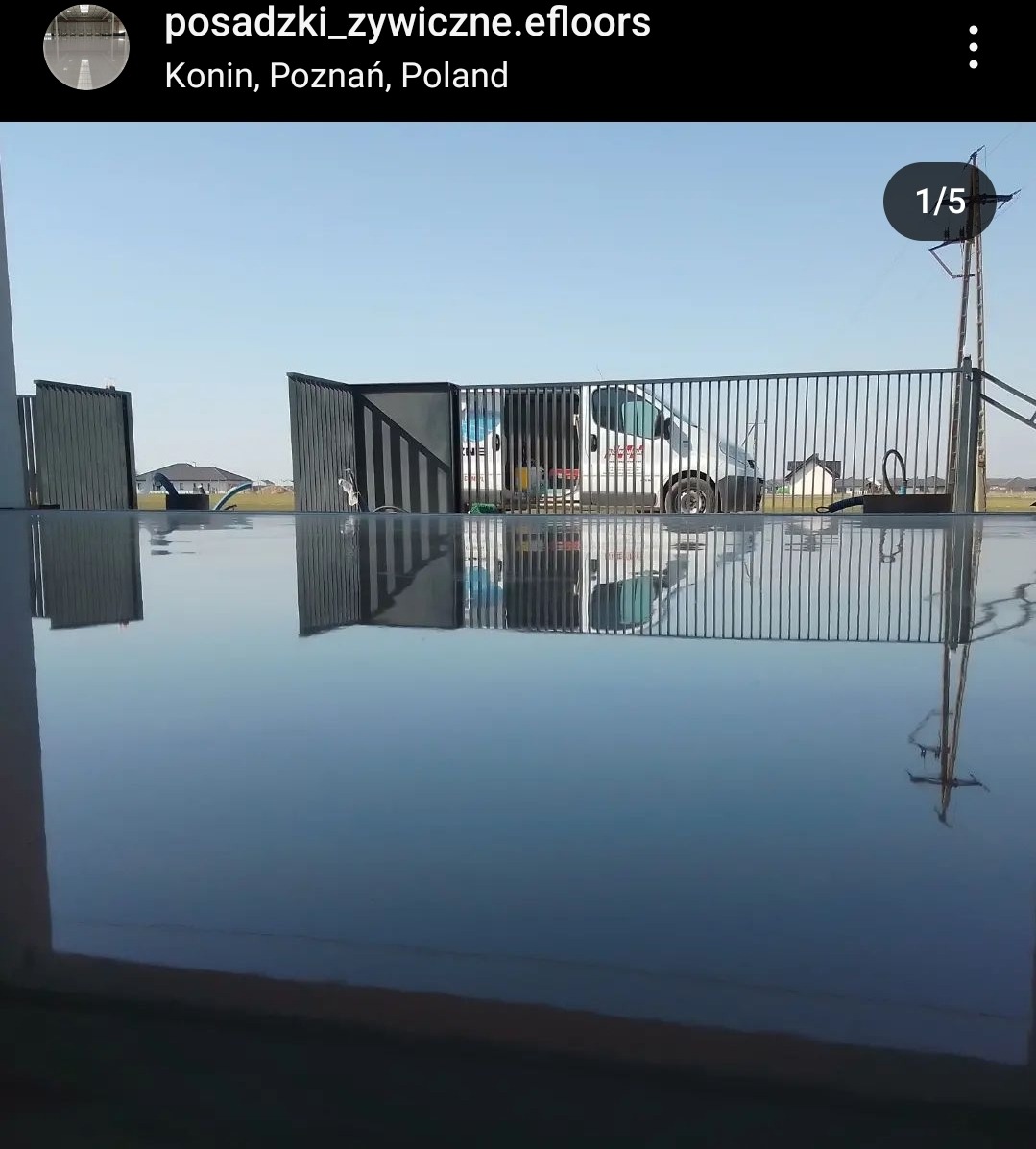 Błyszcząca, szara posadzka żywiczna w Kazimierzu Biskupim, odbijająca ogrodzenie i zaparkowany samochód firmy. Widoczny efekt lustrzanego odbicia.